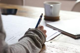 person writing on brown wooden table near white ceramic mug by Unseen Studio courtesy of Unsplash.