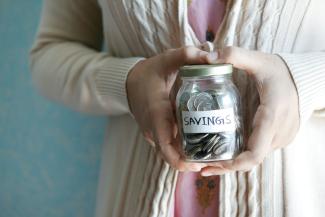 a woman holding a jar with savings written on it by Towfiqu barbhuiya courtesy of Unsplash.